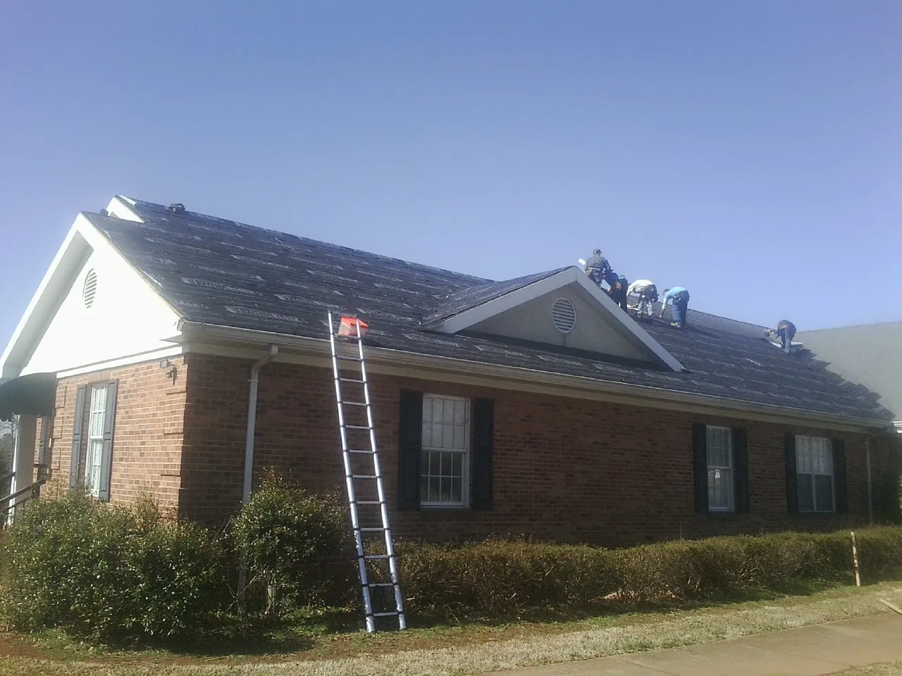 Crew tearing shingles off a brick ranch roof with a ladder set — Metal Roof Repair work by our crew in Roselle