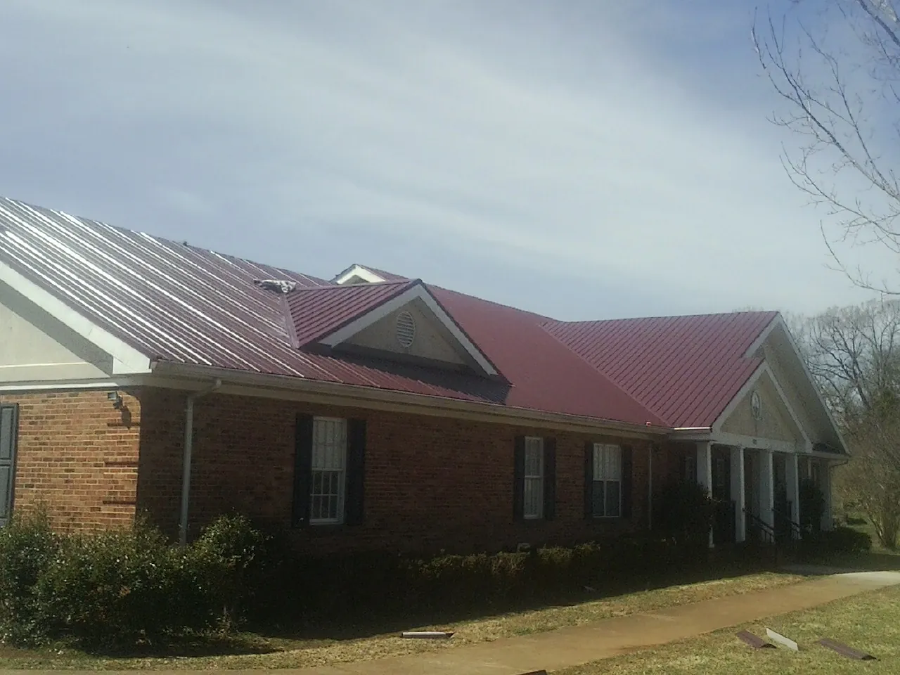 Red metal roof with gabled entries on a long brick building, from a Hail Damage Roof Repair job in Roselle
