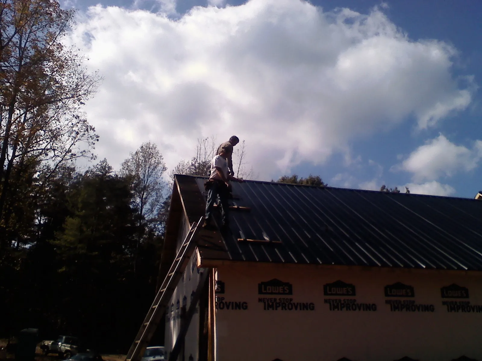 Roofer fastening dark metal panels high against a cloudy sky, from a Roof Inspection job in Roselle